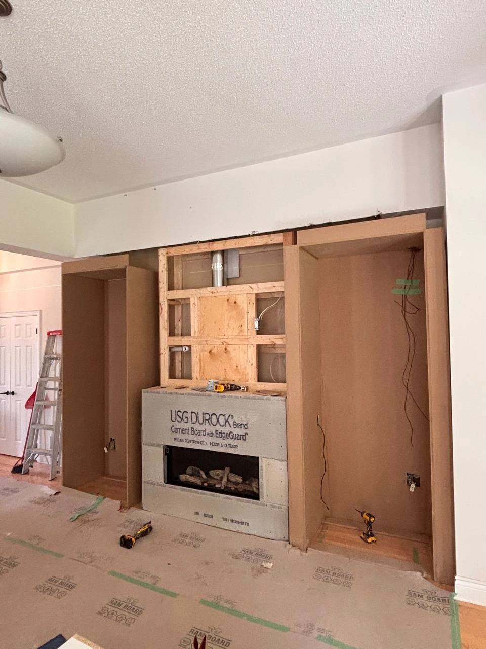 Unfinished cabinet towers being installed on both sides of the retained gas fireplace