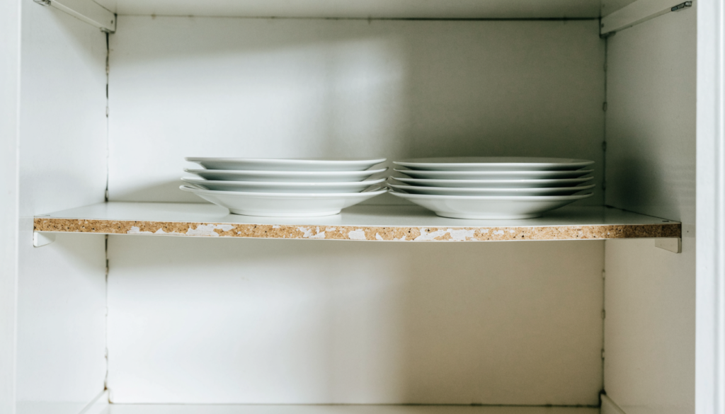 a bowed kitchen cabinet shelf with worn edge banding and stacked plates